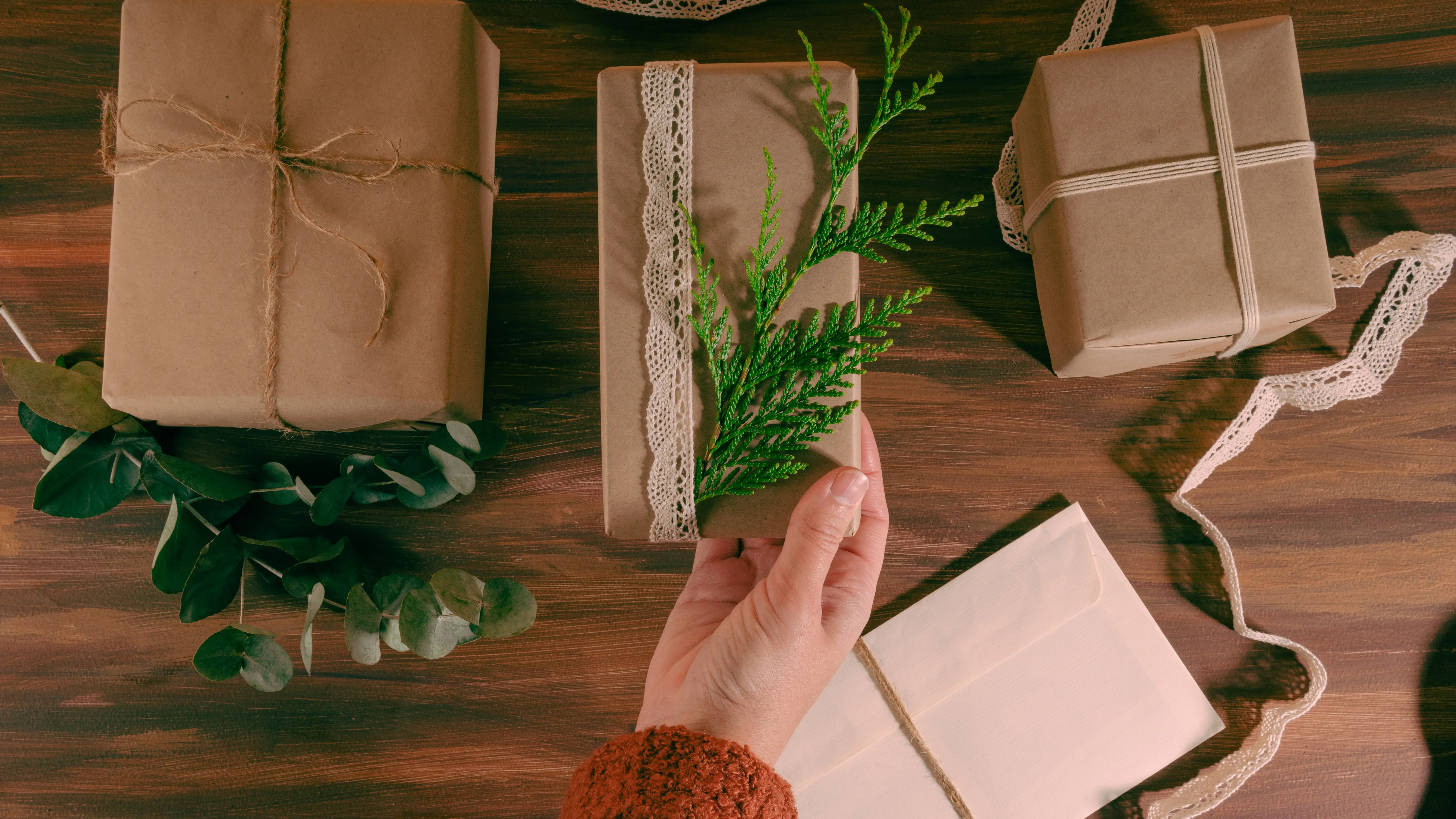 Hand einer Frau hält einen Kiefernzweig über drei Kraftpapier-Schachteln. Horizontale Ansicht.